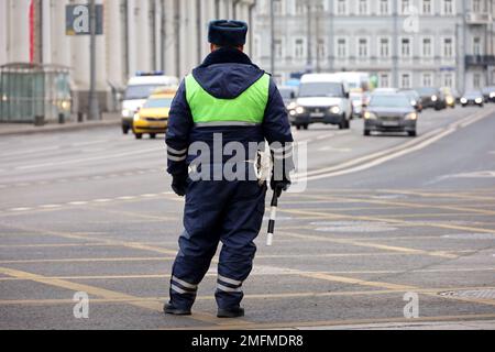 Traffic police officer standing with rod on a road on cars background. Policeman patrol the city street Stock Photo