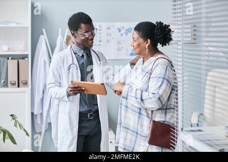 Waist up portrait of young African American doctor consulting female patient using digital tablet in clinic setting Stock Photo