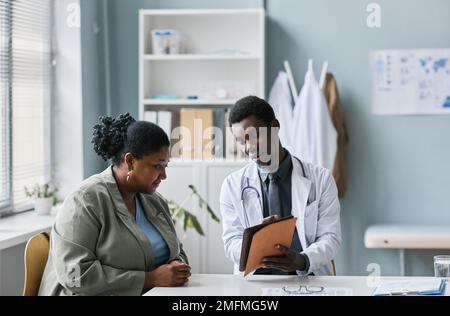 Portrait of young black doctor consulting woman in clinic and pointing at tablet screen, copy space Stock Photo