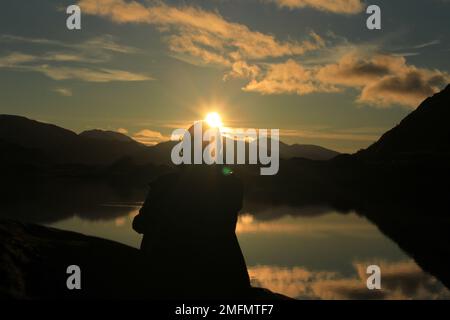 Person sitting and watching gorgeous sunset over the Meeting of the Waters in Killarney National Park in winter. Concept for mindfulness or meditation Stock Photo