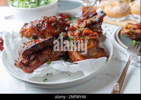 Oven baked thick pork ribs with homemade barbecue sauce, salad and bread for dinner or lunch on a table Stock Photo