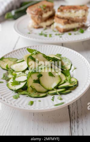 Zucchini salad marinated with olive oil, vinegar and honey. Served as a healthy sandwich side dish on white kitchen table. Front view Stock Photo