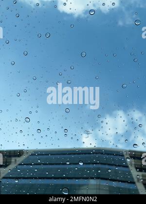 Selective focus on the rain droplets on the glass sunroof of a vehicle with blue sky in the background, after a downpour. Abstract concept. Stock Photo