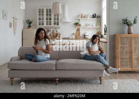 Lonely bored teenage girl sitting on sofa with working online mother, need attention from parent Stock Photo