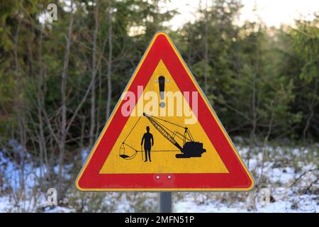 Custom made road sign or traffic warning sign with old excavator and a gentleman with a top hat and cane by rural road in winter. Finland 2023. Stock Photo