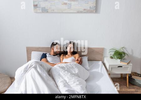 Man in pajama hugging brunette girlfriend in morning in bedroom,stock image Stock Photo