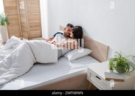 Bearded man hugging girlfriend in pajama while relaxing on bed,stock image Stock Photo