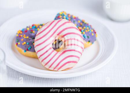 American donuts on white plate on bright background. Playful and colourful image of sweets and desserts. Stock Photo
