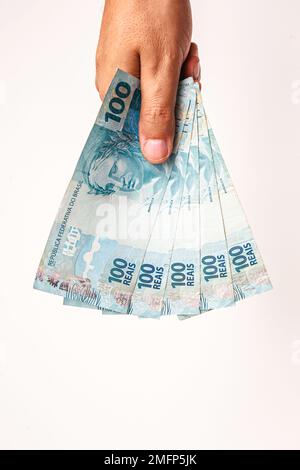100 reais bills from Brazil, held by male hand on isolated white background. Banknotes of one hundred reais from brazil, payday. Stock Photo