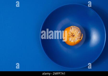 Half peeled tangerine on dark blue plate  Stock Photo