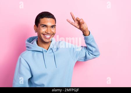 Photo portrait of positive smiling cheerful attractive guy wear blue hoodie showing v-sign peace everyone stop war isolated on pink color background Stock Photo