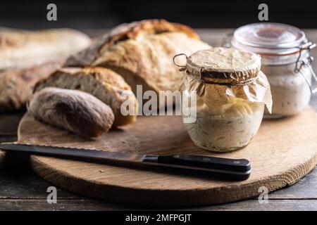Rye sourdough ripened in a jar together with fresh bread on a cutting board. Stock Photo