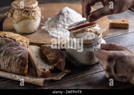 Male hands open a jar with active yeast, fresh bread and pastries in the background. Stock Photo