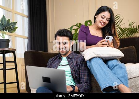 Wide shot of happy smiling couples busy using laptop and mobile phone at home on sofa - concept of technology addiction, cyberspace and digital Stock Photo