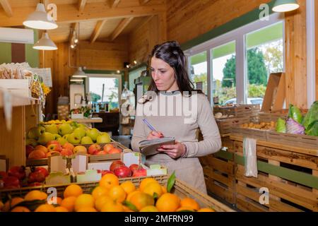 Store manager counts fruits and vegetables in wooden boxes of a grocery store -  Woman in supermarket doing the inventory - small business concepts Stock Photo