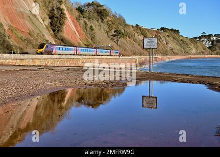 A Cross Country train along the seawall between Hole Head (Parsons tunnel) and Sprey Point, where a warning notice is reflected in a large puddle. Stock Photo