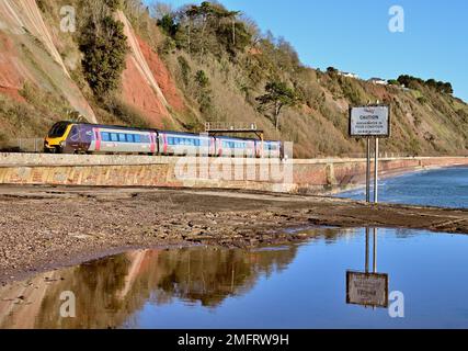 A Cross Country train along the seawall between Hole Head (Parsons tunnel) and Sprey Point, where a warning notice is reflected in a large puddle. Stock Photo