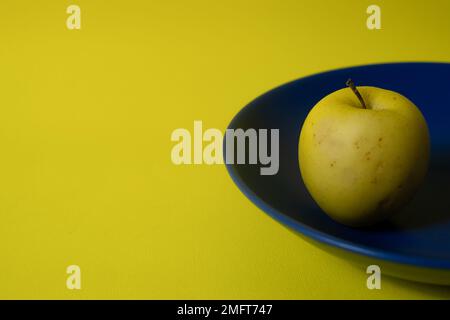 Fresh yellow apple on a blue plate with yellow copy space  Stock Photo