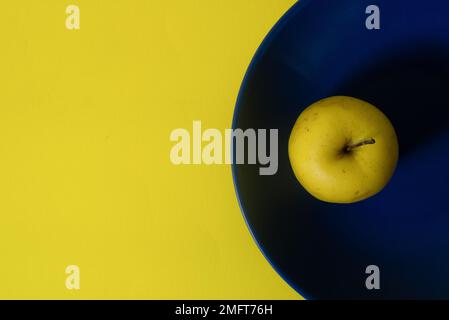 Top view of fresh yellow apple on a blue plate with yellow copy space  Stock Photo