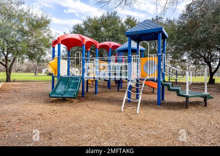 A scene of the colorful children's playground activities in a public park surrounded by trees in the daytime Stock Photo