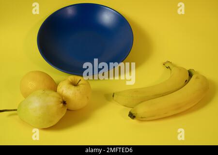 Blue plate on a yellow background with fruits around Stock Photo