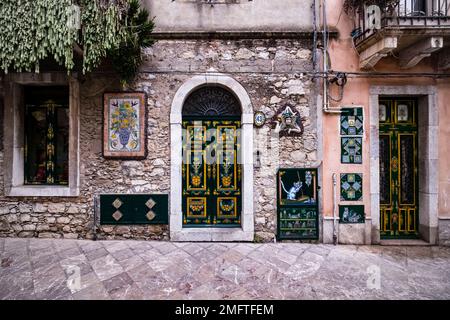 Facade of a house with artfully painted doors and ceramic tiles in one of the alleys of the tourist destination of Taormina. Stock Photo