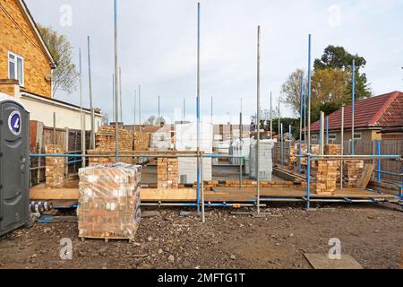Building materials stacked on house construction site work in progress on external detached house cavity walls of facing bricks & insulating blocks UK Stock Photo
