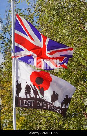 Lest We Forget red poppy remembrance banner flag depicts armed soldiers in silhouette below union jack fluttering in breeze in Essex garden England UK Stock Photo
