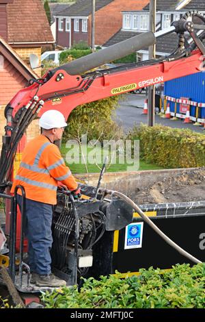 Close up hgv lorry driver standing behind truck cab operating hydraulic controls of bulk grab crane bucket unloading lose trench backfill materials UK Stock Photo