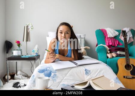 A teenage girl does homework on her bed in her bedroom. Stock Photo