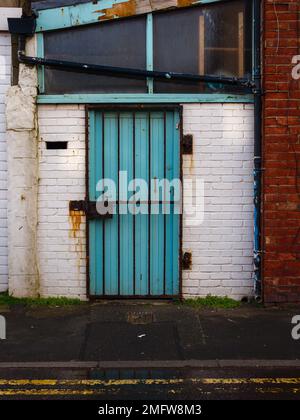 Steel security gate on rear door of scruffy business premises flaky paint and rust stains Stock Photo