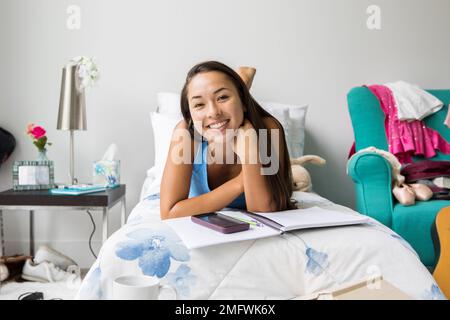 A teenage girl does homework on her bed in her bedroom. Stock Photo