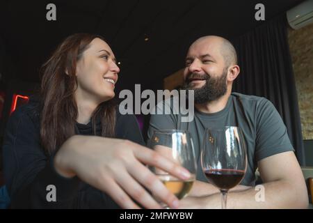 Man and woman drinking white and red wine and looking at each other smiling in a restaurant. Stock Photo