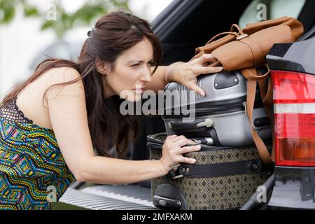 woman struggling to push luggage into car boot Stock Photo