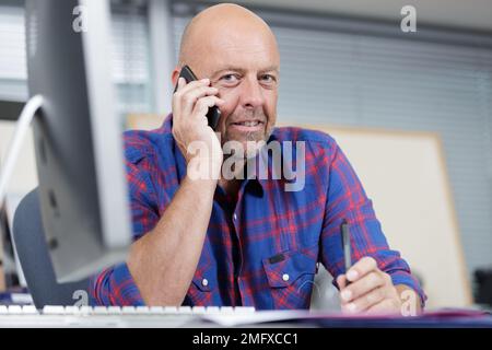 salesman sat at computer desk talking on smartphone Stock Photo