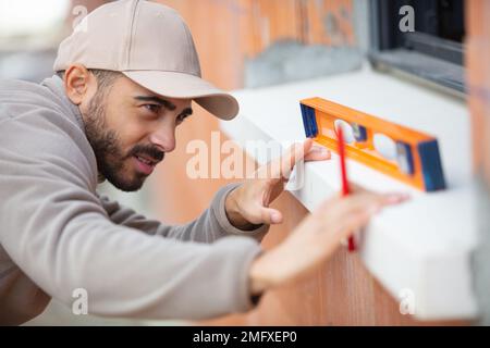 male builder using level tool to measure window outdoors Stock Photo