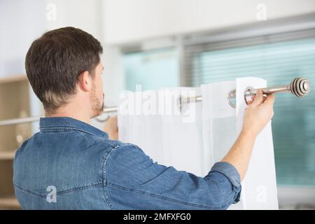 man hanging window curtain indoors interior decor element Stock Photo