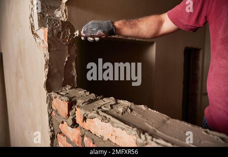 Close up of man hand in work glove laying brickwork in building under construction. Male worker applying cement mortar on bricks with trowel tool. Masonry construction concept. Stock Photo