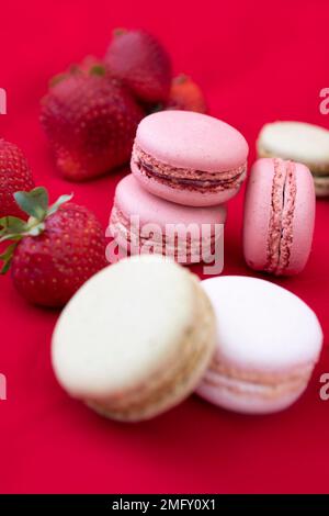 Tasty colourful French macaroon cookies on a red background with strawberries Stock Photo