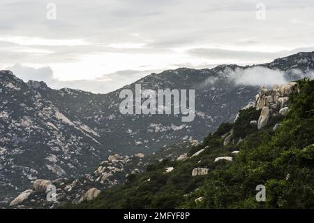 Hilly landscape just outside Phan Rang Vietnam, with cloudy skies on a partially sunny day with the mountains sloping down to the sea Stock Photo