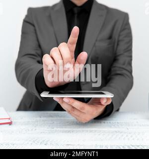 Businessman in gray jacket sitting at table holding mobile phone And Pointing With One Finger On Important Message. Gentleman Showing Critical Stock Photo