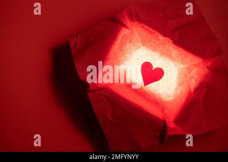 Close up of a hand cut heart made from paper inside of a red box with a back light for effect Stock Photo