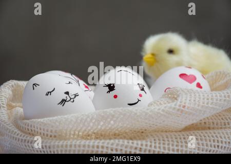 Easter eggs lie in mesh bag. Yellow chick sits on eggs on dark background. Funny peaks and twig with red flowers are drawn. Copy space. Happy Easter Stock Photo