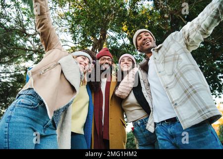 A group of multiracial young friends having fun together in a park doing autumn weekend activities wearing coats and hats. Five happy people smiling and walking outdoors. Lifestyle concept. High quality photo Stock Photo