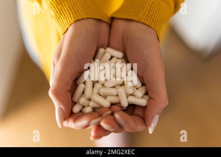 From above of crop unrecognizable depressed woman in casual wear demonstrating handful of pills on blurred background at home Stock Photo