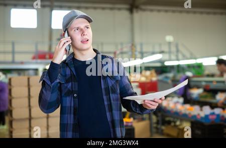 Young fruit factory foreman with papers talking on phone Stock Photo