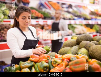 Supermarket woman worker in black apron putting vegetables in her department Stock Photo