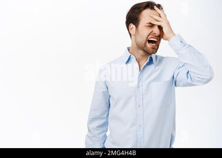 Frustrated man grieving, screaming and holding hand on head. Businessman having headache, migraine, standing over white background Stock Photo