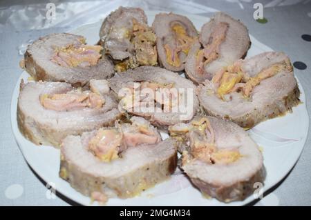 Close up of rolled pork roast served on a big white plate on a grey dining table. Stock Photo