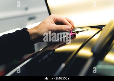 Close-up shot of unrecognisable man hand removing small dent in car using bright lamp in a garage. Professional car repair and detailing. Horizontal indoor shot. High quality photo Stock Photo